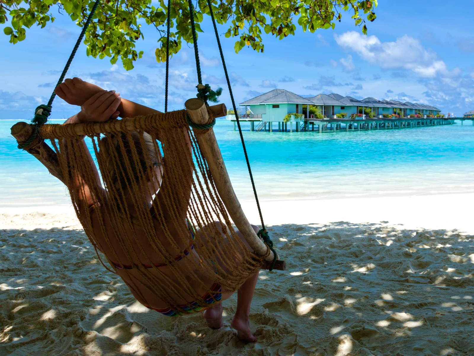 Woman sitting in a hanging chair in the shade for a piece on the best time to visit Jamaica and looking at villas across the way