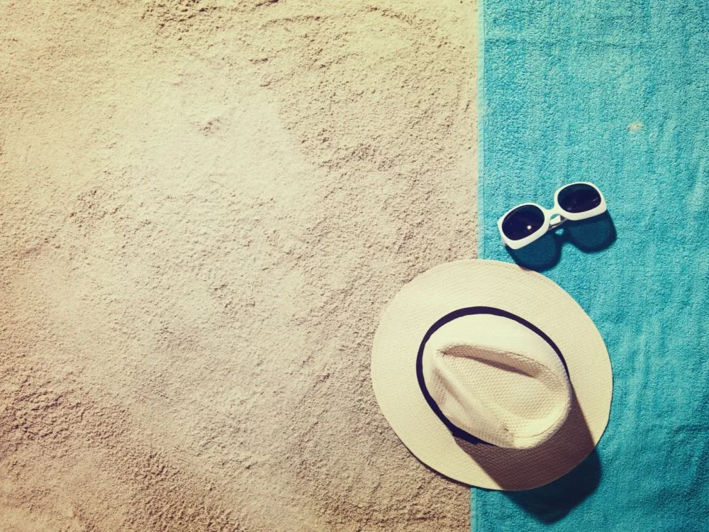 The best travel towel on a beach with a cream colored hat and sunglasses on it