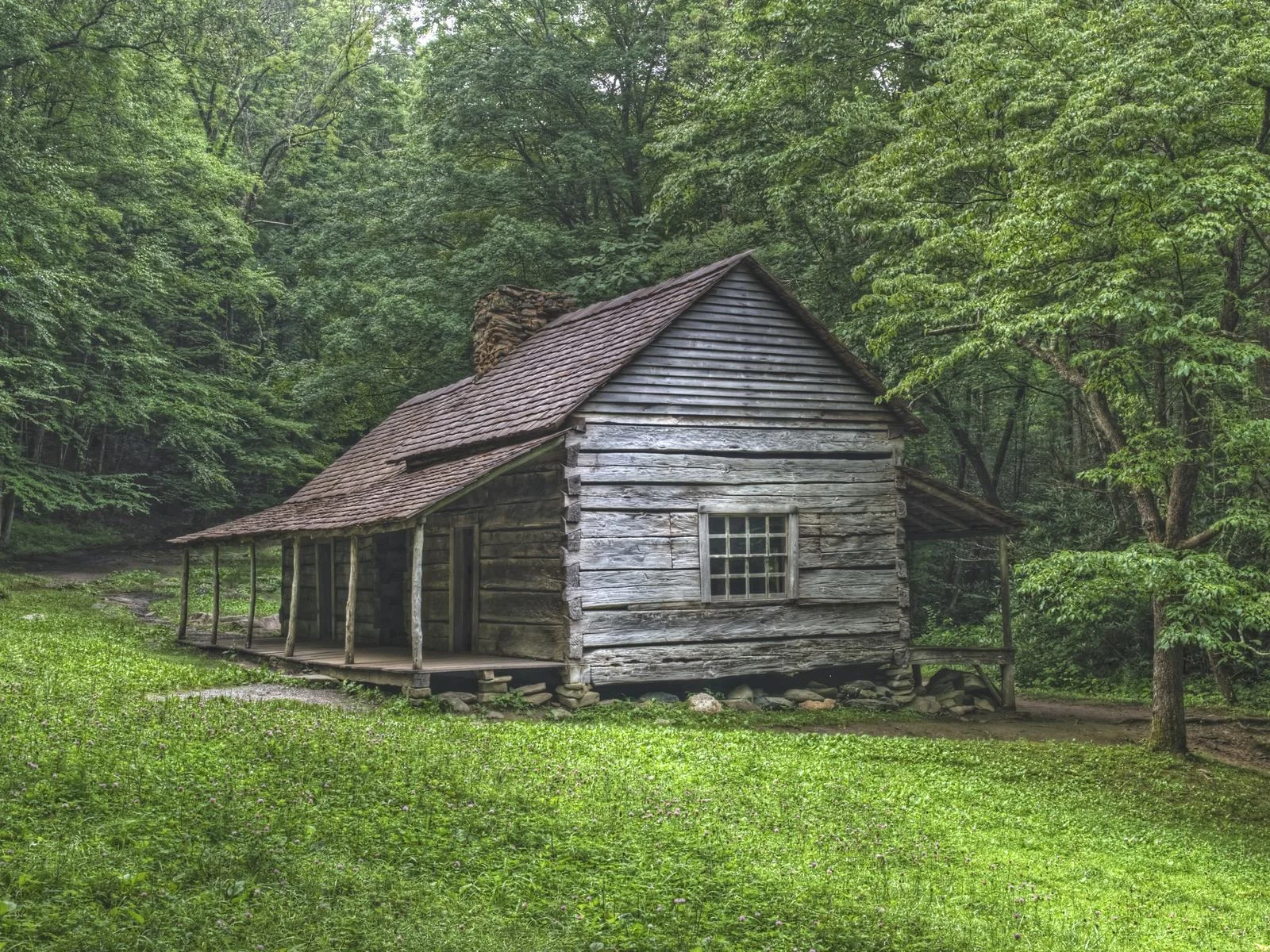 the historic and old-looking ogle log cabin is one of the best things to do in gatlinburg, tennessee, which only has one window and is surrounded by green grass and trees with thick leaves
