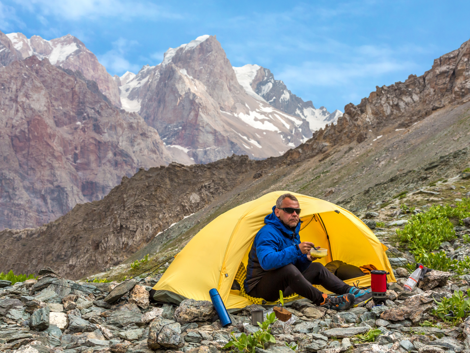 Cool older man with grey hair on the side of a mountain in the best one-man tent (yellow in color) drinking coffee