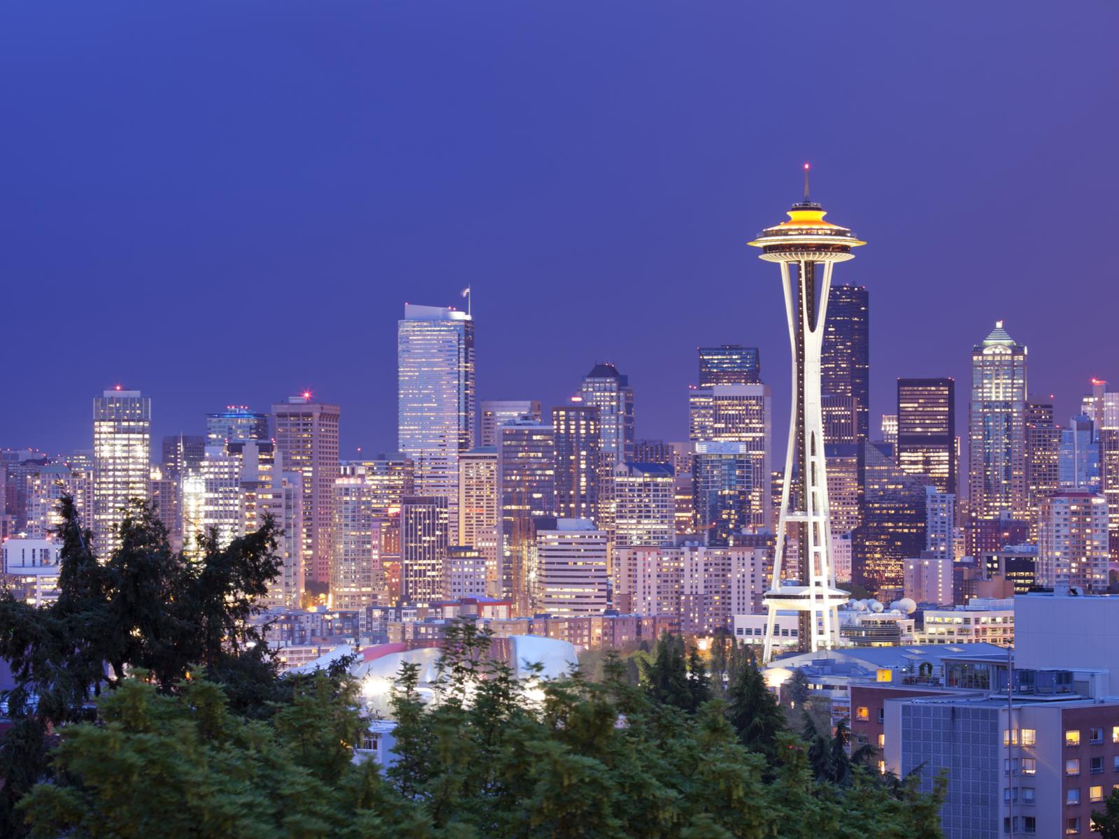 The Space Needle in Seattle, Washington is one of the most iconic places in America, standing above other structures and the Seattle skyline at night in background