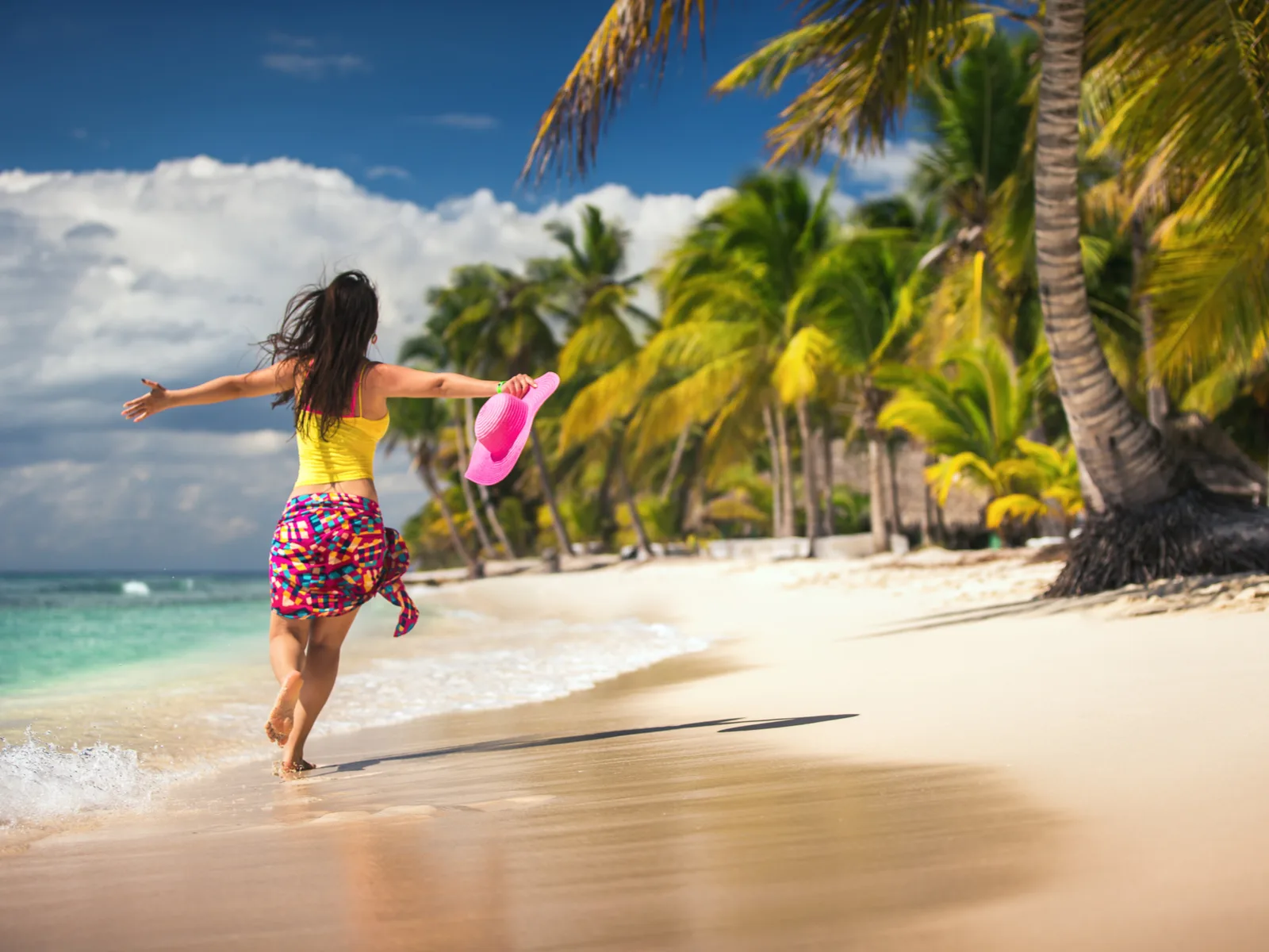 Carefree woman in a yellow shirt running along the beach next to palm trees during the best time to visit Punta Cana