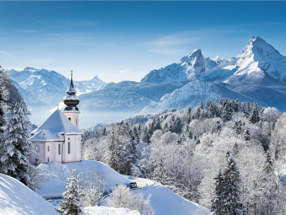 Panoramic view of the Alps overlooking the mountains with a church in the foreground during the worst time to visit Germany, in Winter