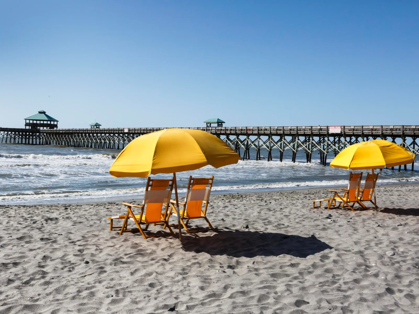 Empty yellow beach chair under umbrellas beside the famous tall boardwalk at Folly Beach in South Carolina, one of the best beaches on the East Coast