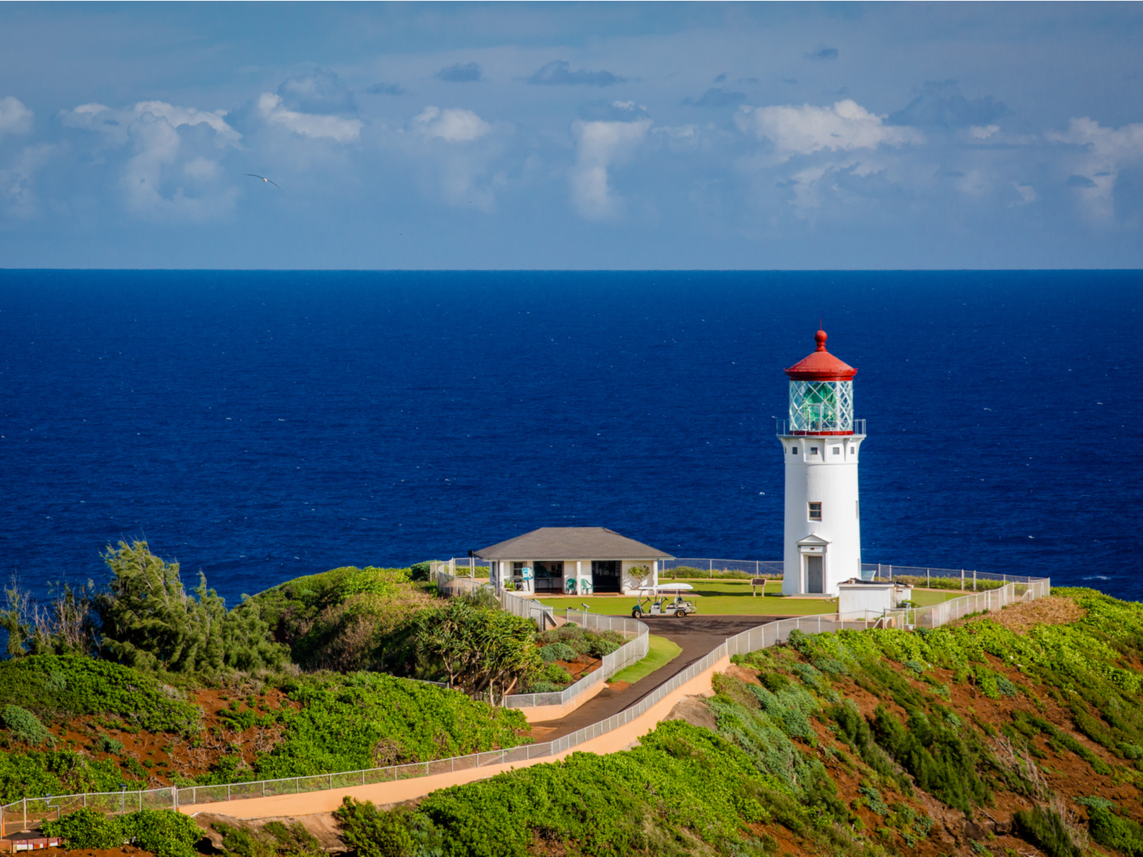 The Kilauea Lighthouse with a house and a gulf cart sits beside a blue calm open sea, one of the best things to do in Kauai