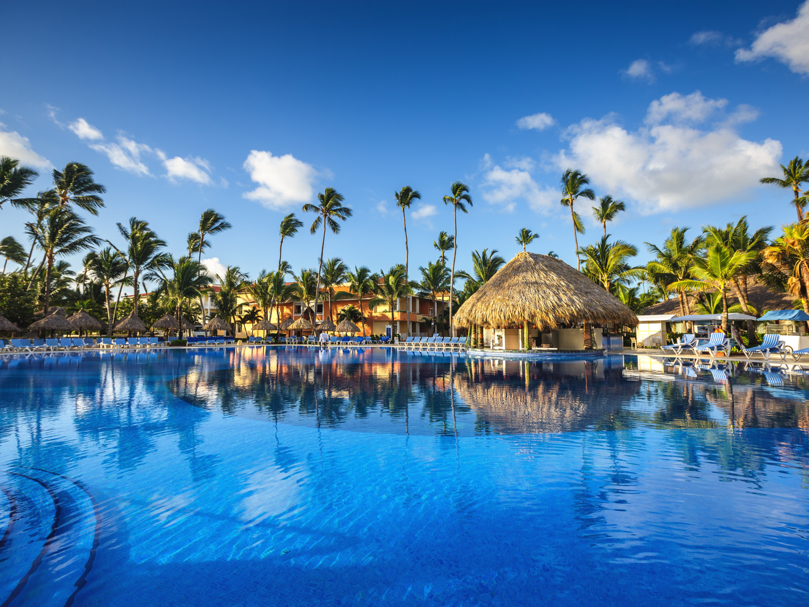 A native hut and tall palm trees reflected on the clear blue pool in one of the best all-inclusive resorts in Punta Cana