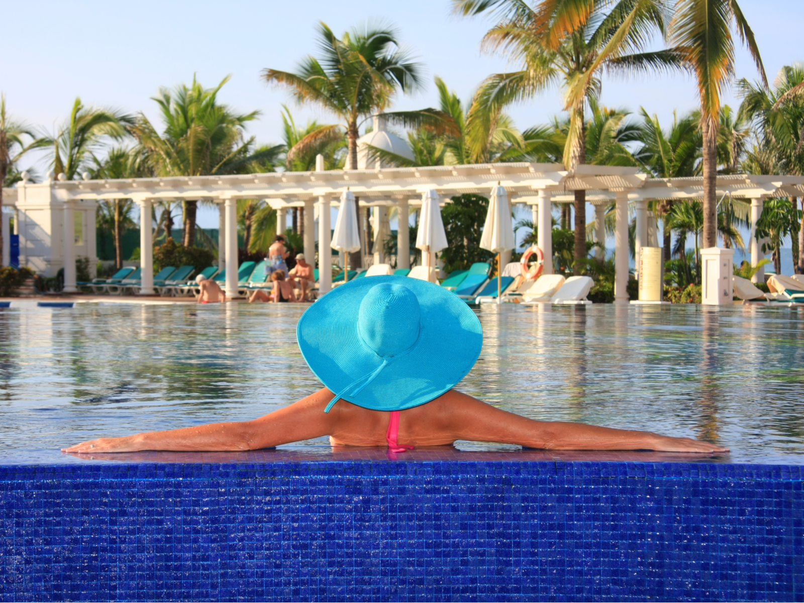 A mature woman wearing her sun hat relax by the edge of a swimming pool in one of the best all-inclusive resorts in Mexico