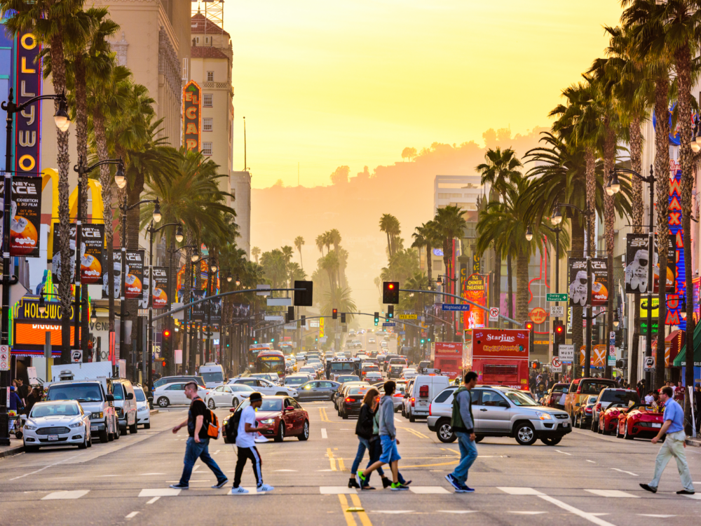 Pedestrians crossing Hollywood Boulevard in the famous theater district with busy traffic in the background during sunset, one of the best things to do in California