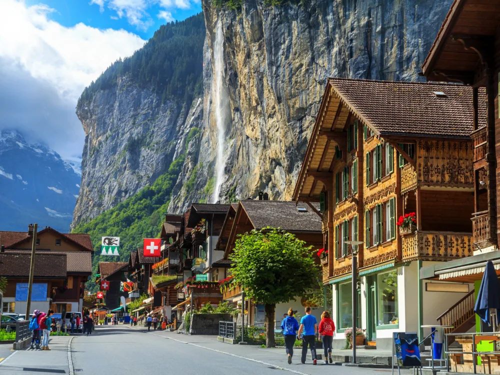 Street of Lauterbrunnen with a waterfall in the background pictured during the cheapest time to visit Switzerland