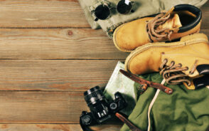 Boots, a camera, and a hiking camera backpack in a layflat image on a wooden table