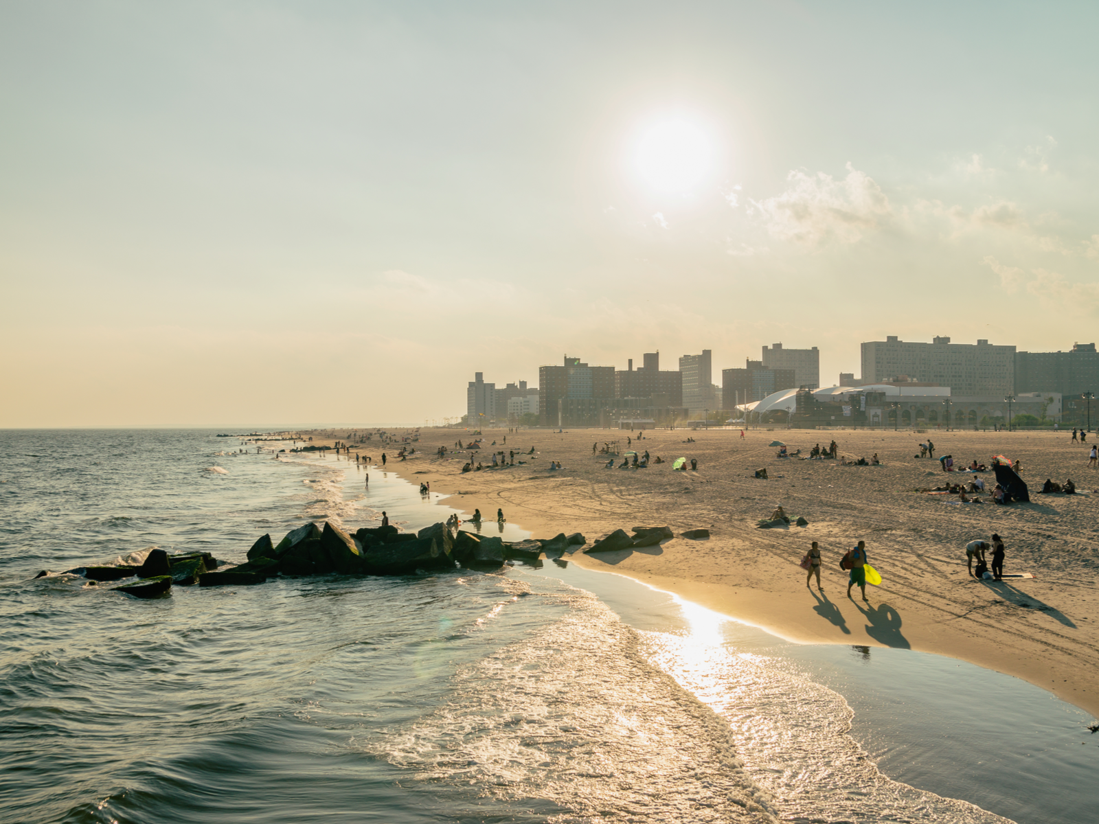 The golden hour over Brighton Beach in New York where people are enjoying the shore and the cityscape in background, one of the best beaches on the East Coast