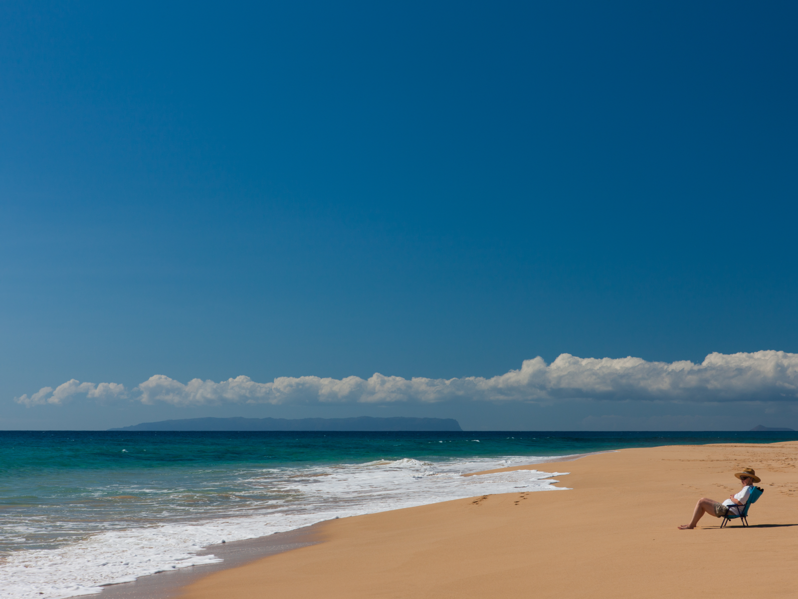 Lone woman in a beach chair watching the waves at Kekaha Beach, one of Kauai's best beaches