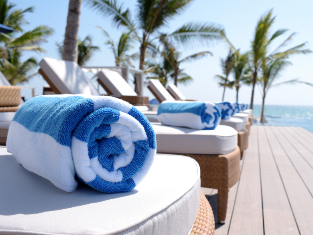 The best travel towels rolled up on sunbeds by the pool on a composite pool deck