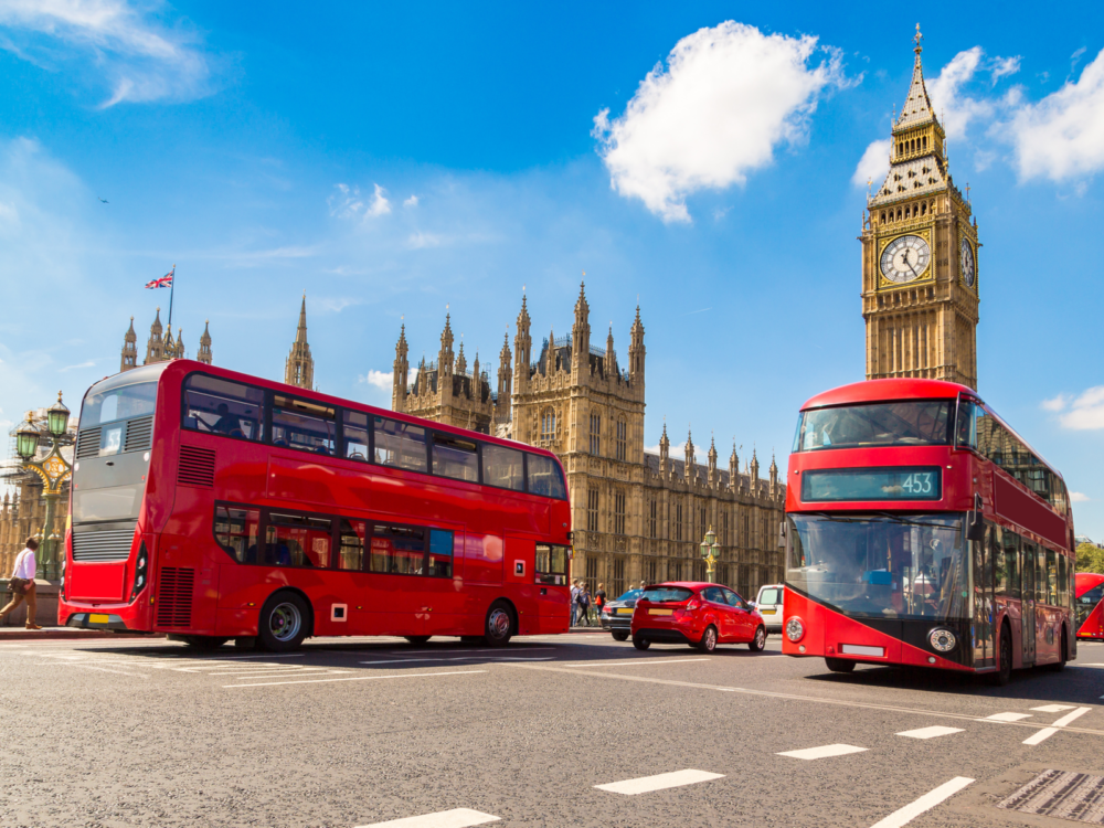 Red double-decker busses driving by Big Ben during the best time to visit London on a sunny day