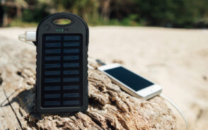 One of the best solar power banks upright on a log charging an iPhone