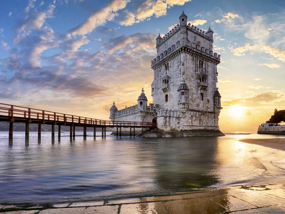 Old Belem Tower on the Tagus River pictured during the cheapest time to visit Portugal with the sun setting in the background