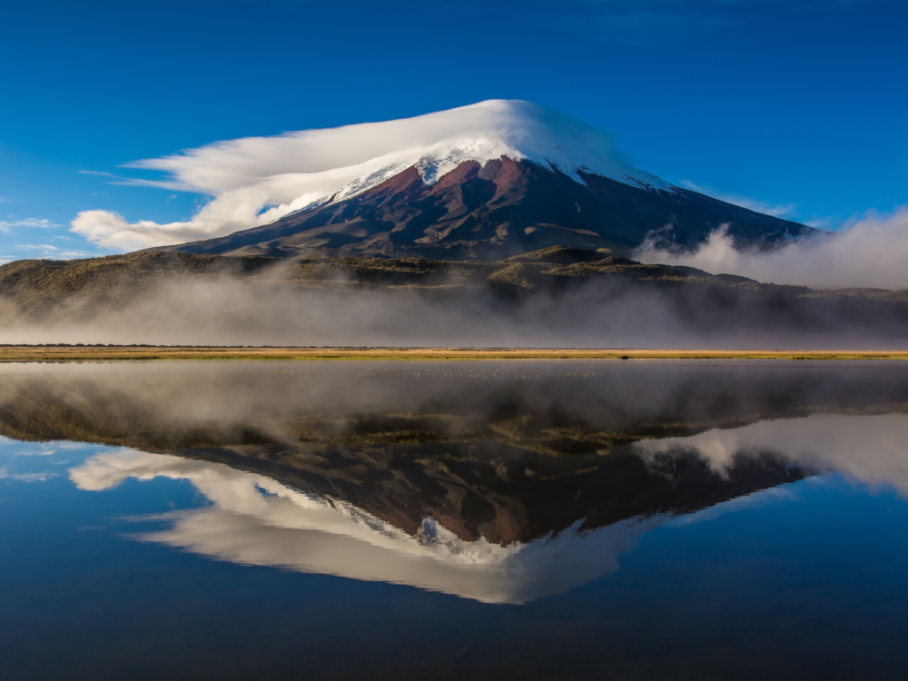 Volcano Cotopaxi overlooking a calm body of water for a piece on the Cheapest Time to Visit Ecuador