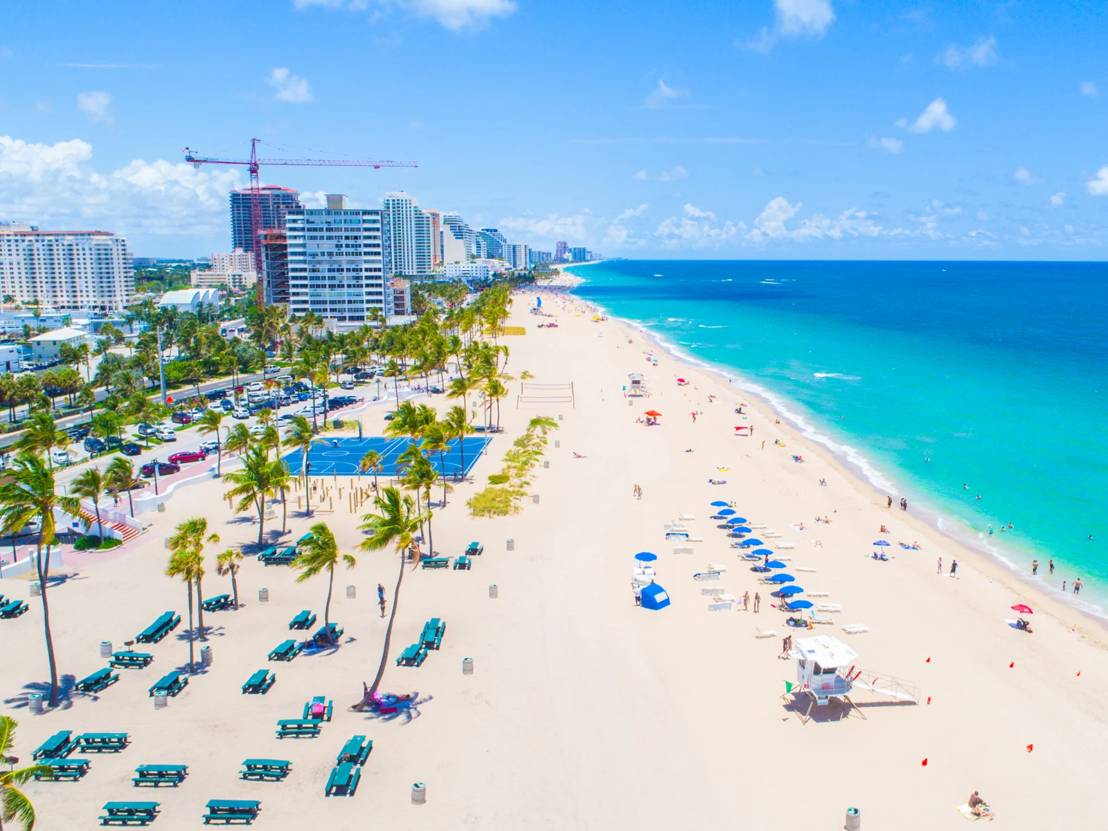 Aerial photo showing the whole span of Fort Lauderdale Beach, one of the best things to do in Fort Lauderdale, with few beach goers, vacant benches, palm trees, and blue water