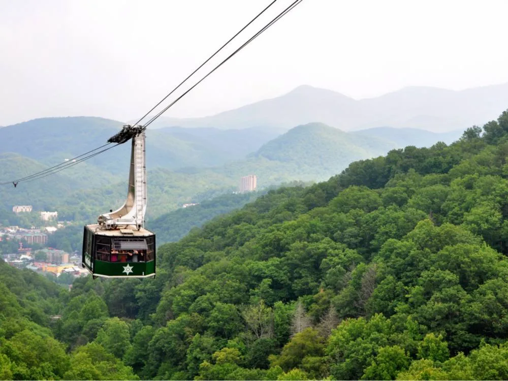 people riding a green gondola at ober gatlinburg arial tramway with scenic overlooking view of tall mountains and pristine forest, one of the best things to do in gatlinburg, tennessee