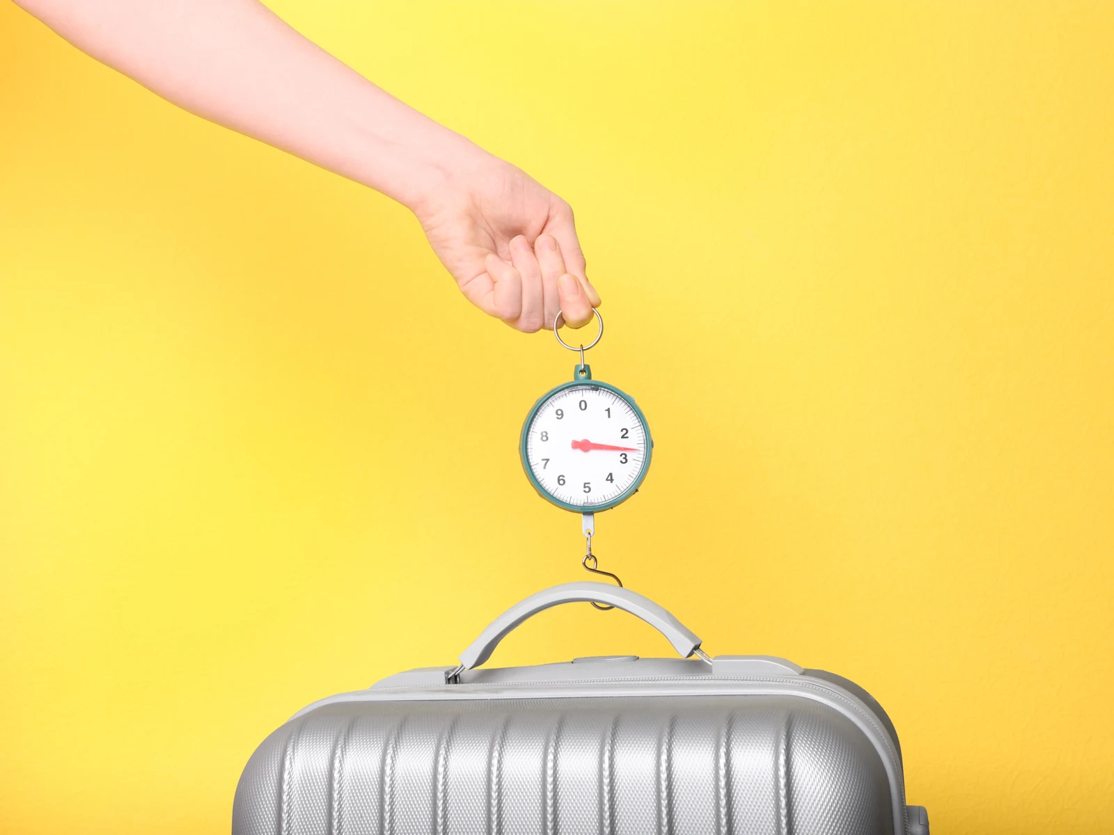 Silver suitcase hanging from the best luggage scale being held by a hand in a yellow room