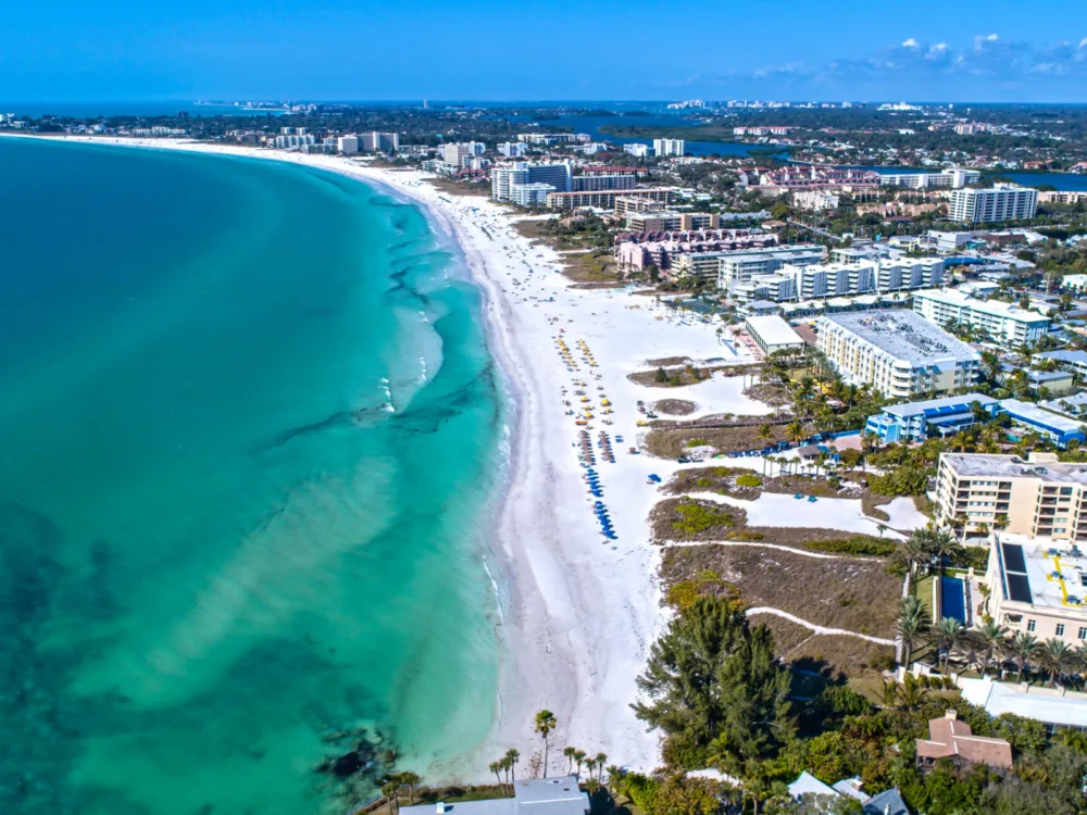 Aerial shot on the white long shoreline of Siesta Beach in Florida, a piece on the best beaches in the US, with its emerald waters and hotels lining up along the beach
