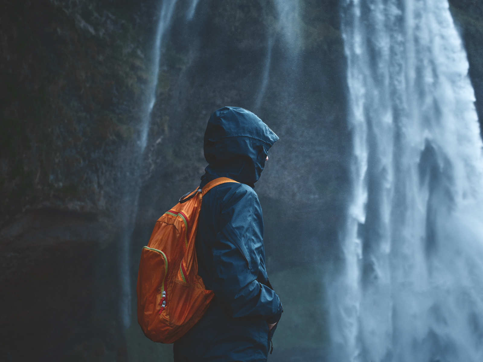 Hooded figure standing in front of a waterfall on a rainy day wearing the best waterproof backpack