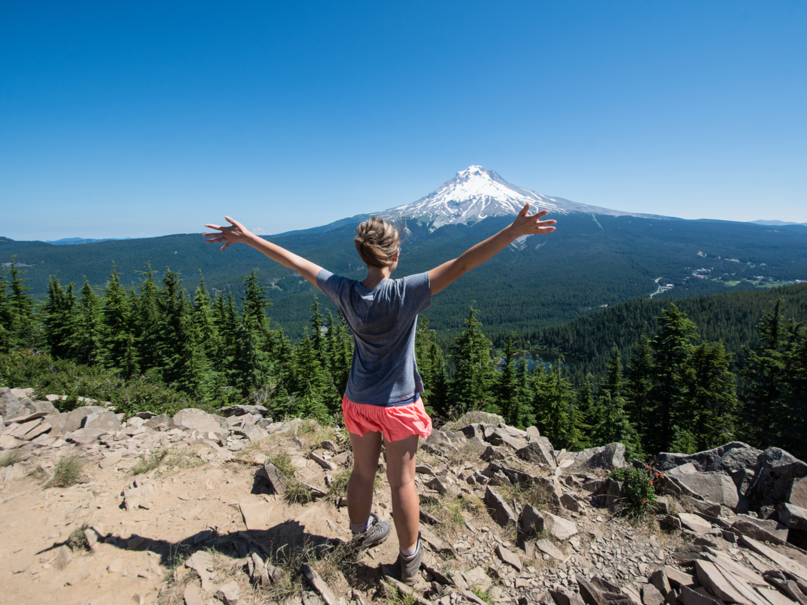 Photo of a woman hiking a mountain in shorts and throwing her hands up during the cheapest time to visit Oregon