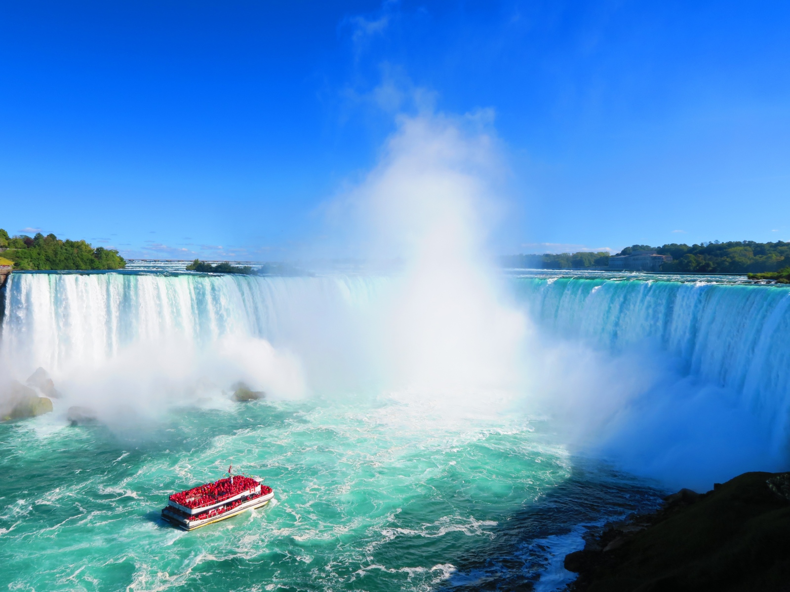 A red touring boat nearing the majestic Niagara Falls, considered as one of the most iconic places in America