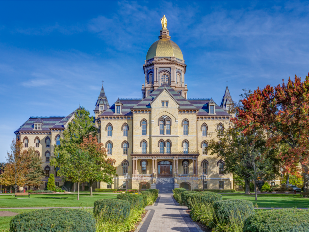 A grand building at the University of Notre Dame du Lac in Indiana, considered as one of the most beautiful college campuses, with a golden statue at its roofing and fronting a wide green grounds