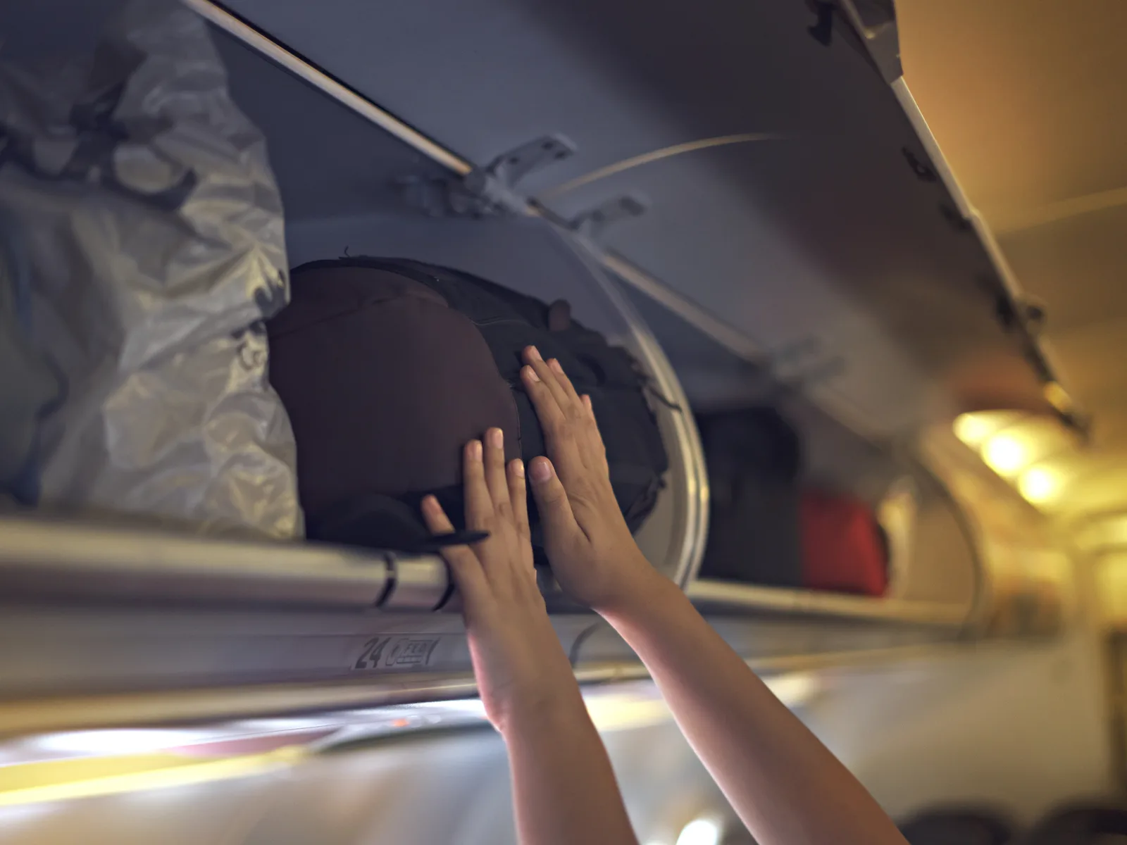 Person loading one of the best carry-on backpacks into an overhead bin in an airplane