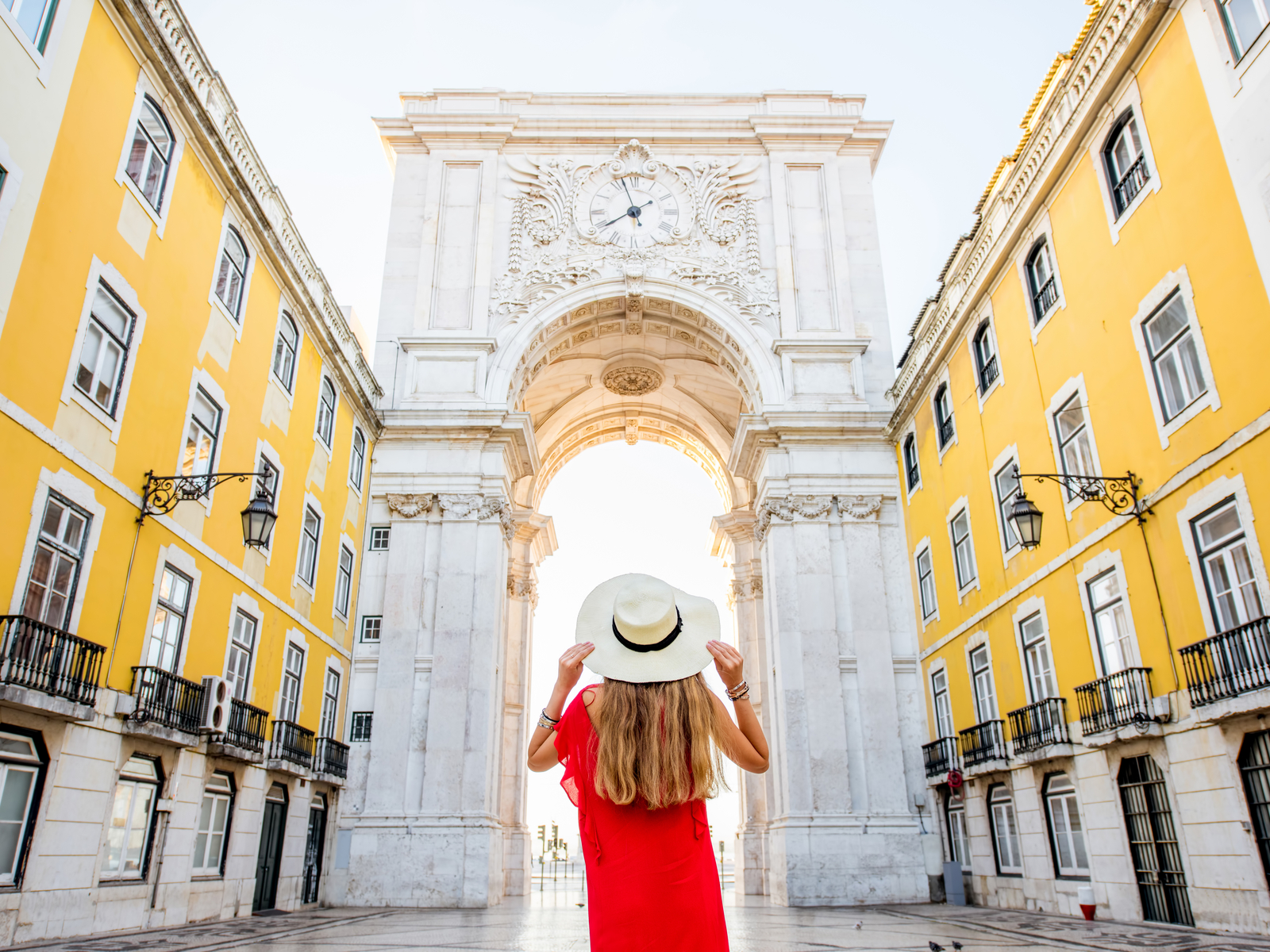 Young woman in a red dress gripping her hat in front of the arch in Lisbon City during the best time to visit Portugal