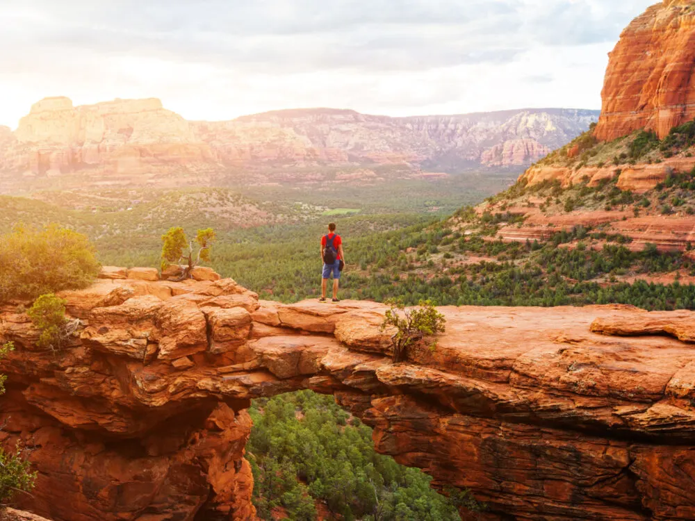 Man standing on Devil's Bridge Trail during the best time to visit Sedona with the sun rising on his left