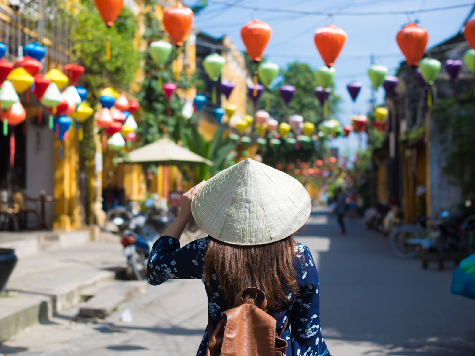 Woman waring a traditional pointy straw hat and looking down the market alleyway for a piece on the best time to visit Vietnam