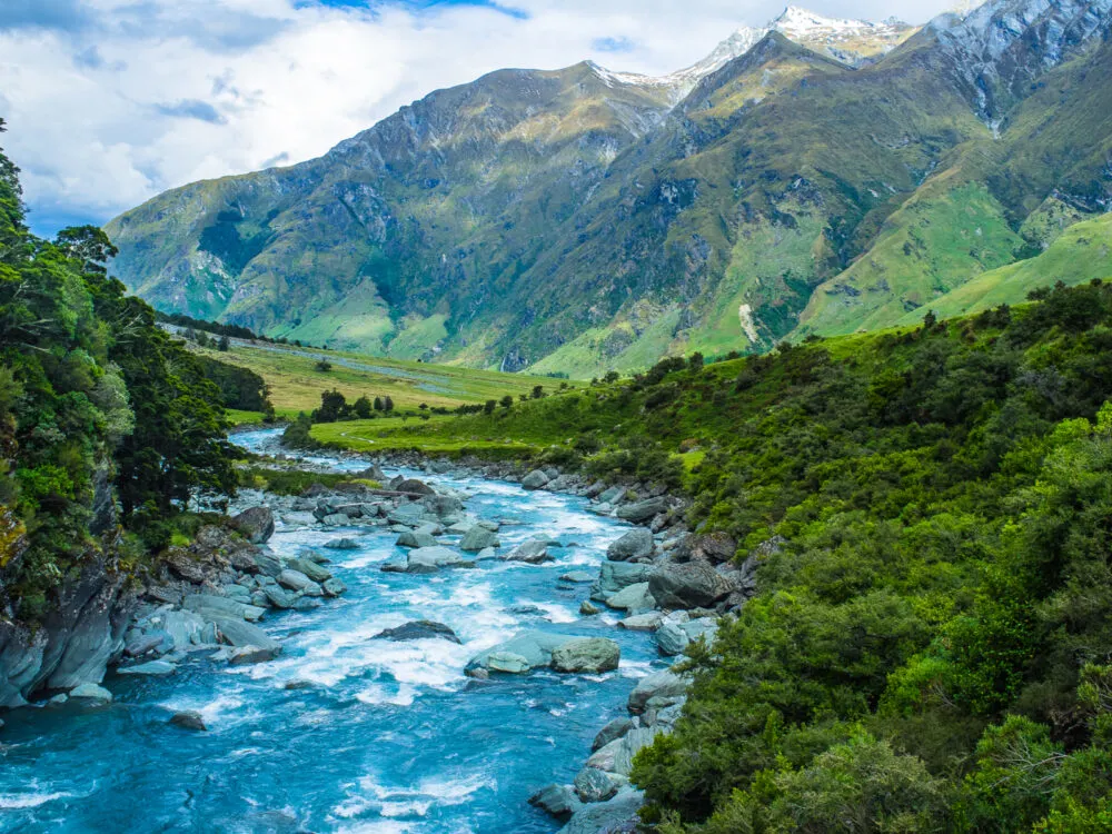 A turbulent winding stream flowing towards the tall Mount Aspiring National Park with it icy peaks, one of the most iconic Lord of the Rings filming locations