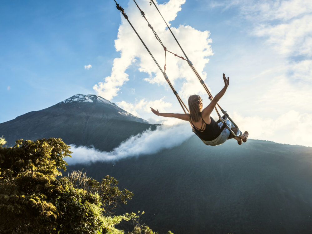 Woman on a swing in Banos with the volcano in the background for a piece titled Is Ecuador Safe to Visit