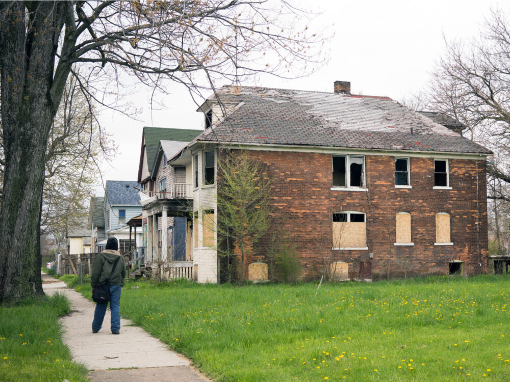 Anonymous person walking along a sidewalk in a bad neighborhood with boarded up homes for a piece on whether Detroit is safe