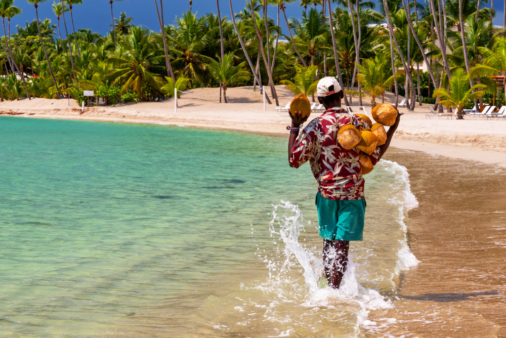 Coconut merchant walking through water next to a beach for a guide to whether or not the Dominican Republic is Safe