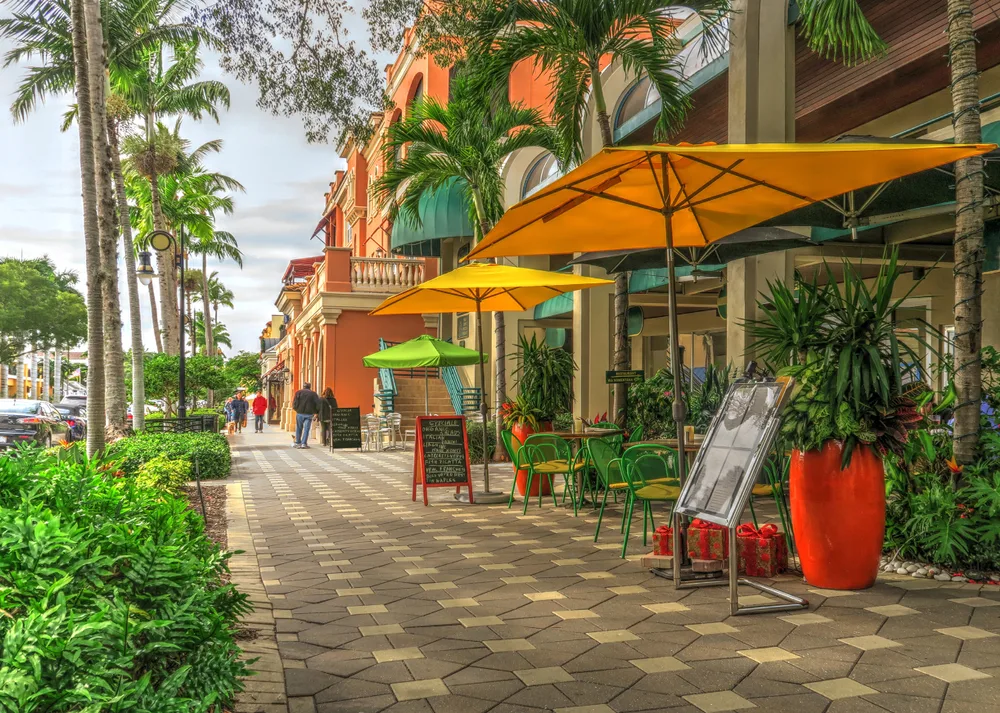 Brick walkway with palm tree-lined streets and umbrellas pictured for a guide titled Is Naples Florida Safe