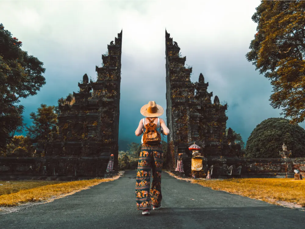 Tourist woman walking with a backpack between the temple gates for a post titled Is Bali Safe