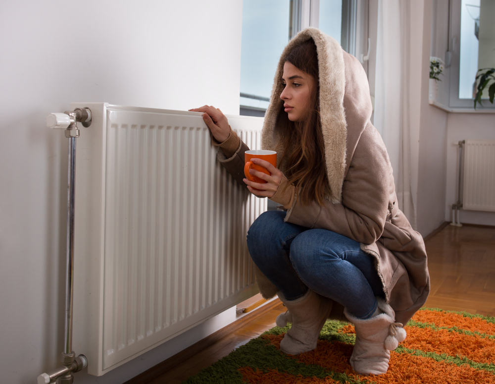 Woman crouching next to a heater instead of wearing the best womans heated jacket