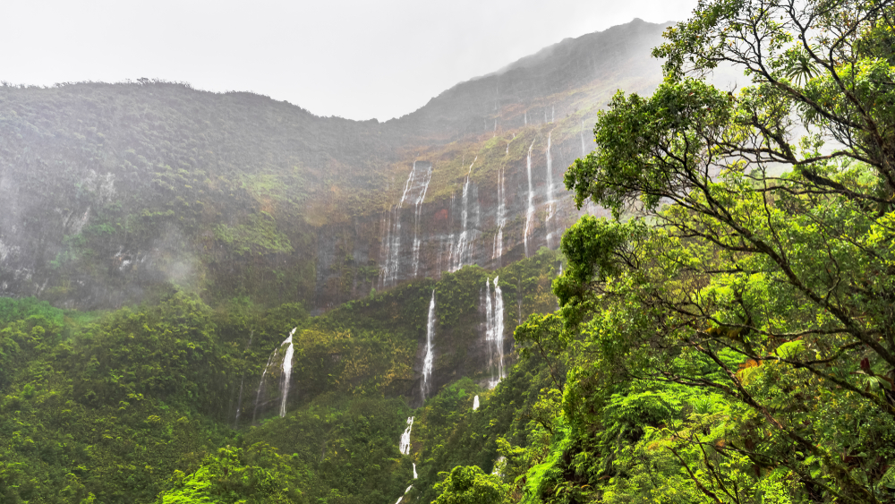 Wall of waterfalls trickling down a mountain in Tahiti with mist and steam surrounding the lush rainforest for a frequently asked questions section detailing the best time to visit Tahiti