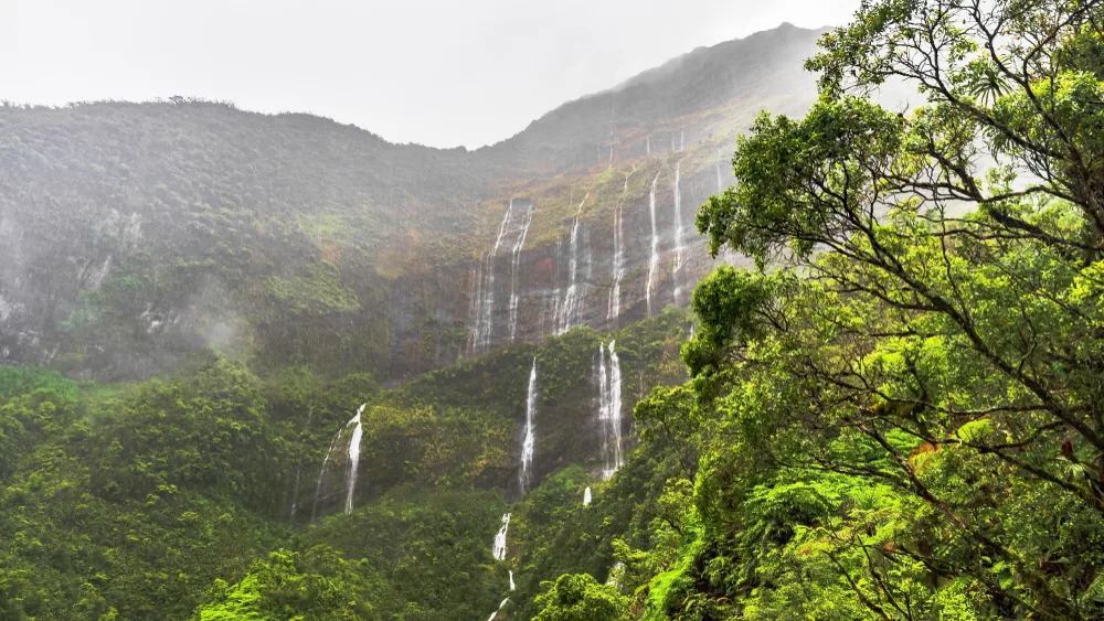 Wall of waterfalls trickling down a mountain in Tahiti with mist and steam surrounding the lush rainforest for a frequently asked questions section detailing the best time to visit Tahiti