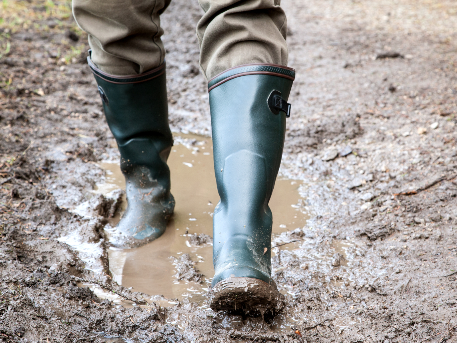 Person with rubber waterproof boots for men walking on a muddy and wet path
