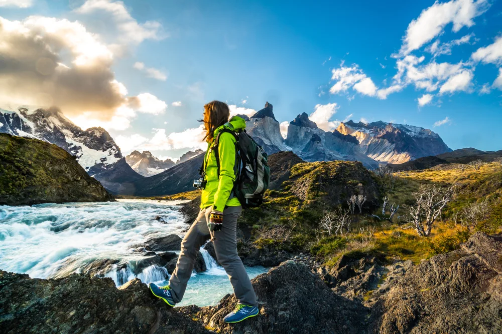 Woman hiking in the mountains during the best time to go to Patagonia with a stream on her right