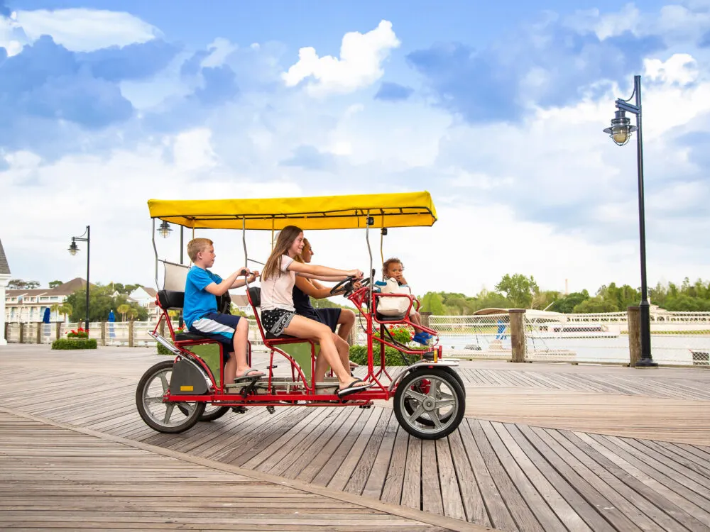 Happy folks on a pedal bike riding on a boardwalk during the cheapest time to visit Orlando