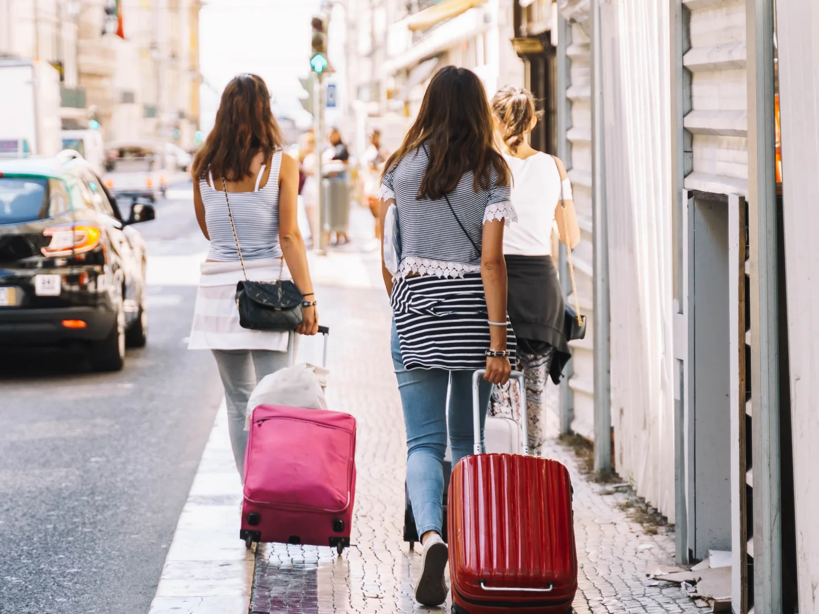 Two women walking on a sidewalk pulling the best backpacks with wheels and wearing casual travel outfits