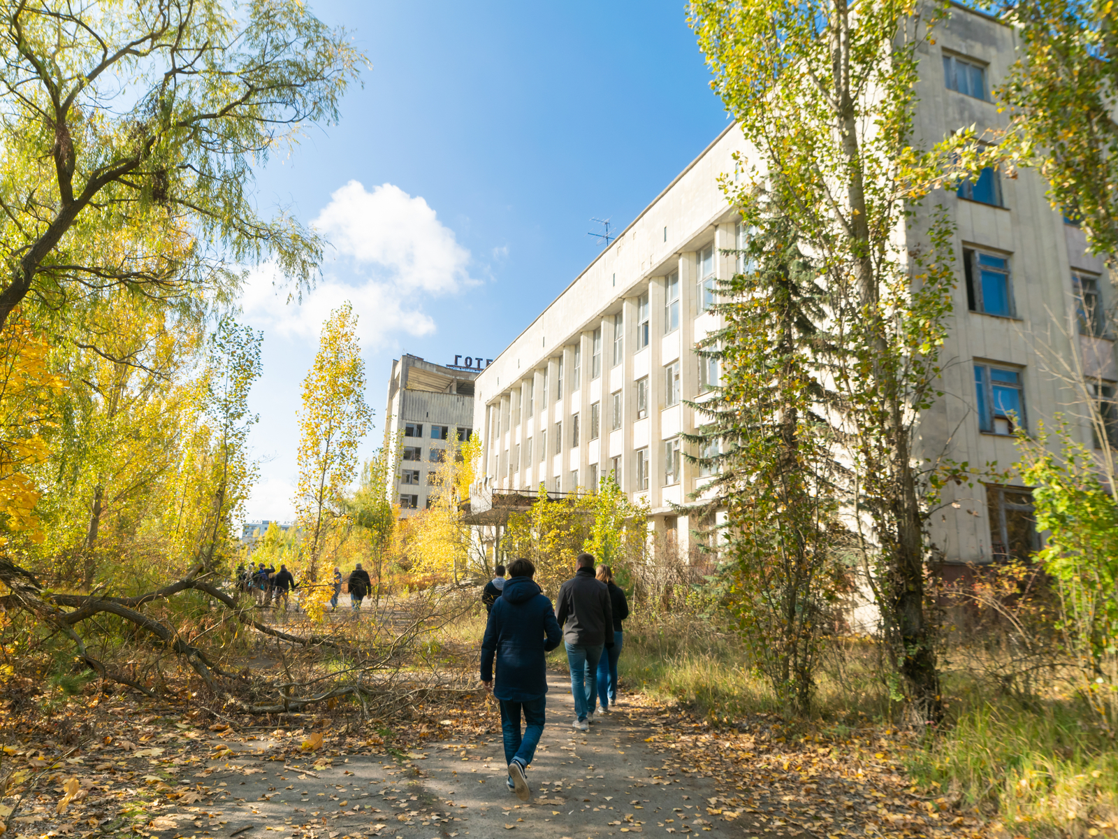 For a piece titled Is Chernobyl Safe to Visit Now, Walking tourists in exclusion zone in Pripyat area and fallen trees on the way in autumn. Dangers and safety conception in Pripyat. Chernobyl tour. Ukraine.08.10.2019