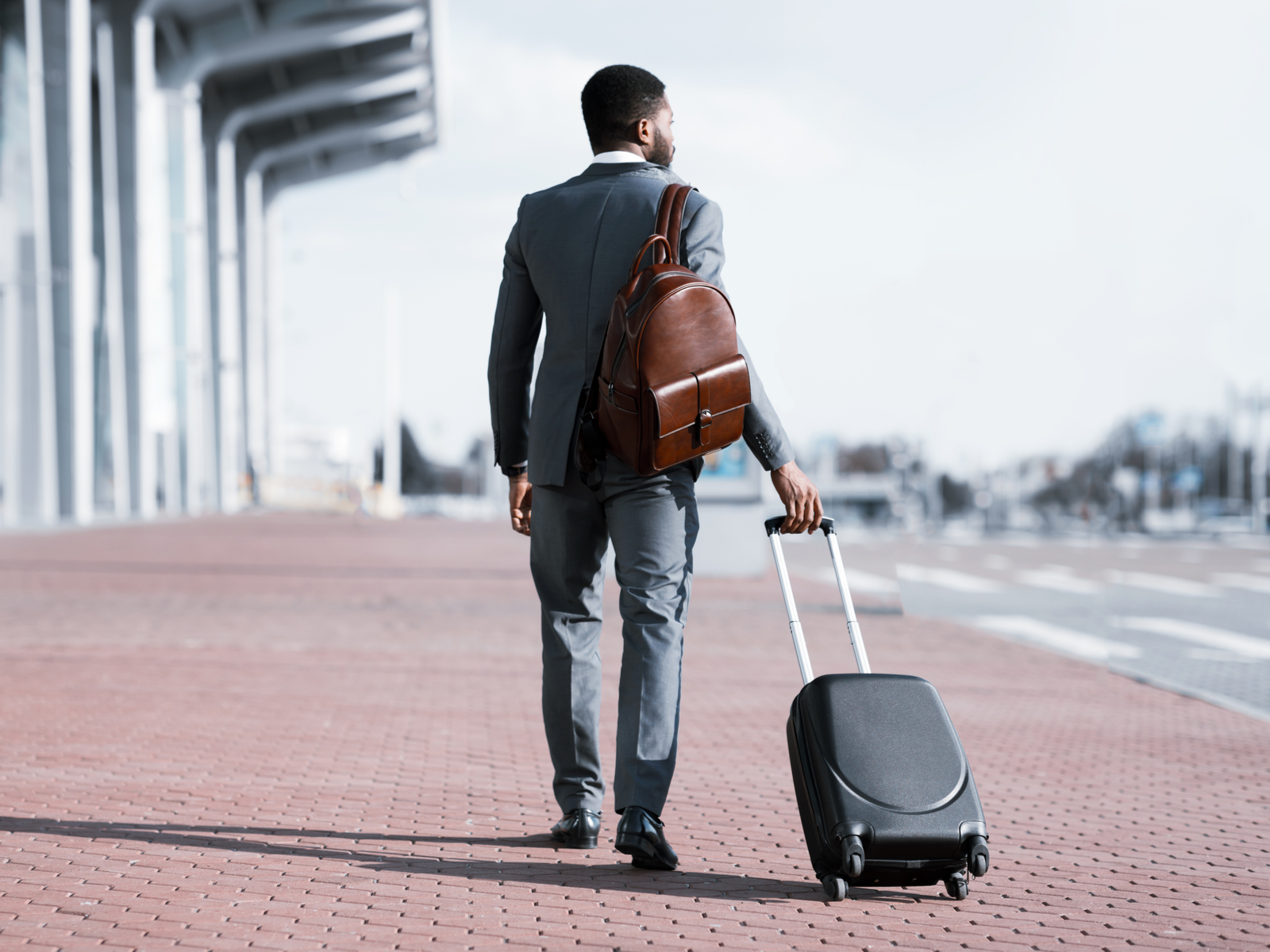 Man in a suit pulling a suitcase and wearing one of the best business travel backpacks that's leather and brown in color