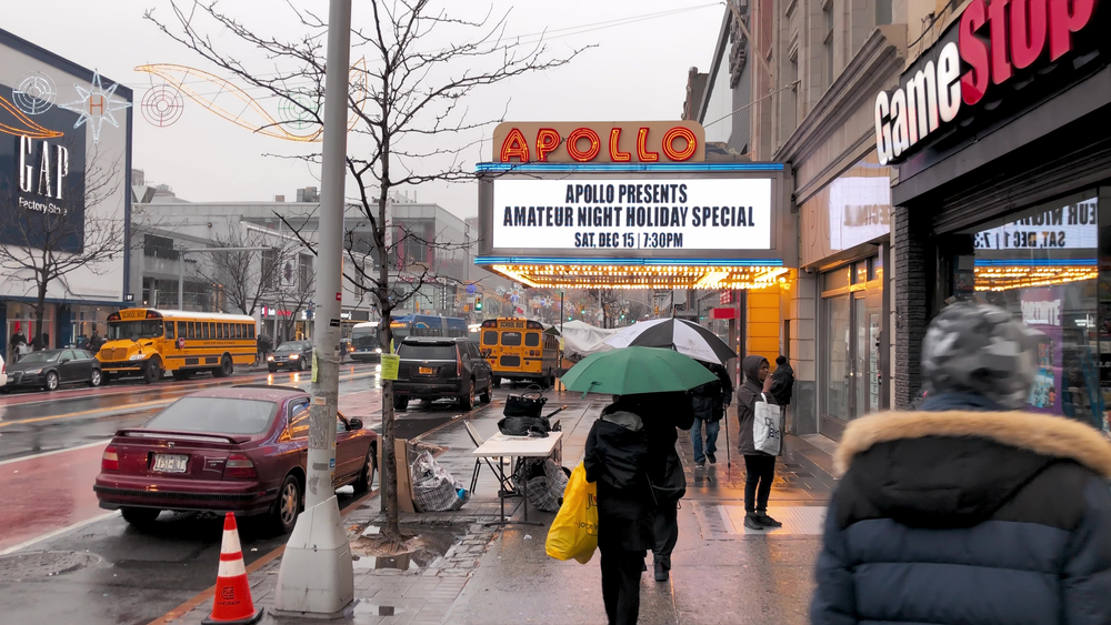 People walking on the streets on a rainy day for a piece on Is Harlem Safe to Visit
