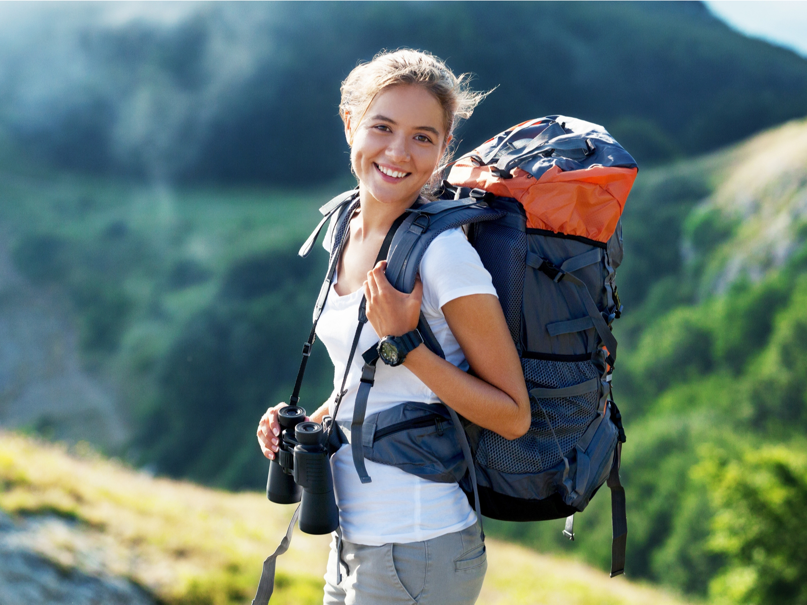 Woman holding the straps of one of the best travel backpacks for women while also holding binoculars